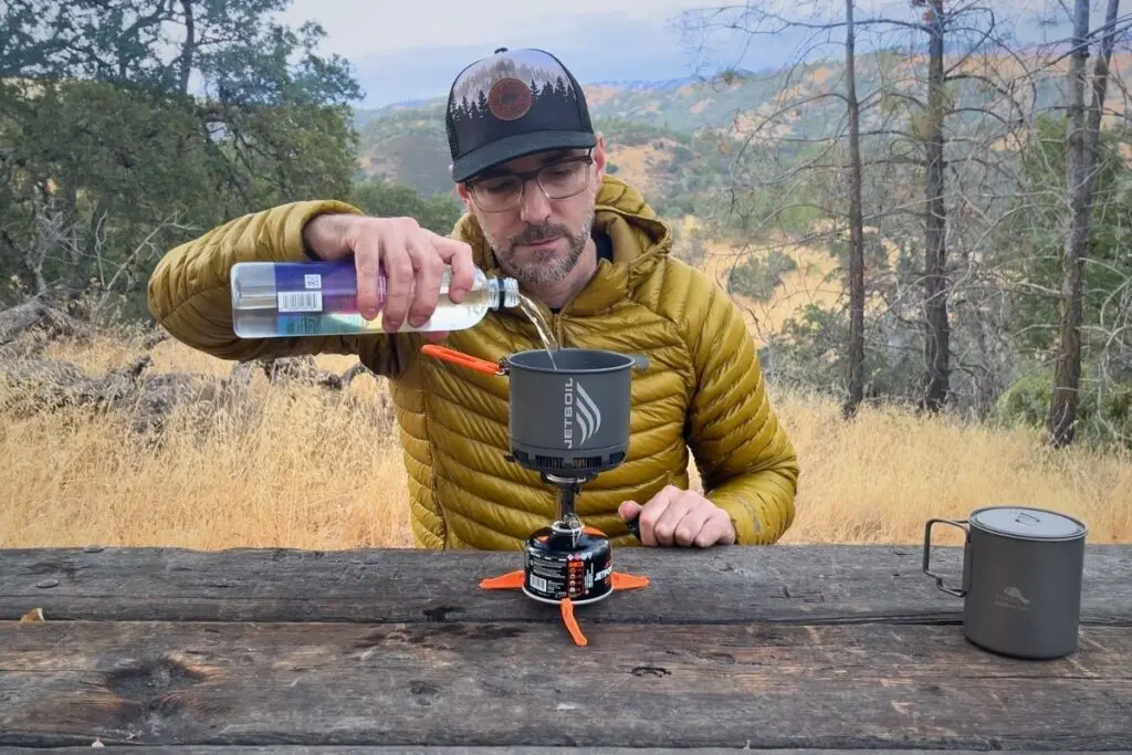using-jetboil-stash-backpacking-stove Pouring water into a Jetboil Stash integrated backpacking stove system at a picnic table with oak foothills in the background.