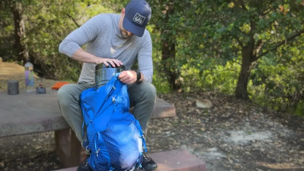 backpacking-bear-canister-fit-in-backpack Backpacker fitting a bear canister into the main compartment of a backpacking pack