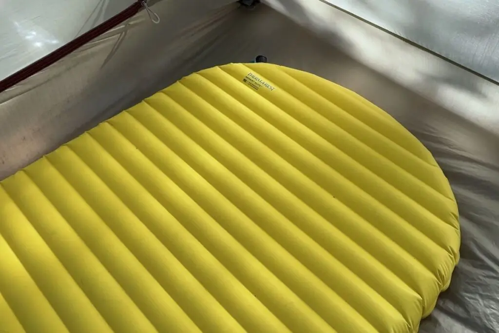 backpacking-sleep-pad-baffle-design Close-up of a yellow inflatable backpacking sleeping pad showing horizontal baffle construction inside a tent