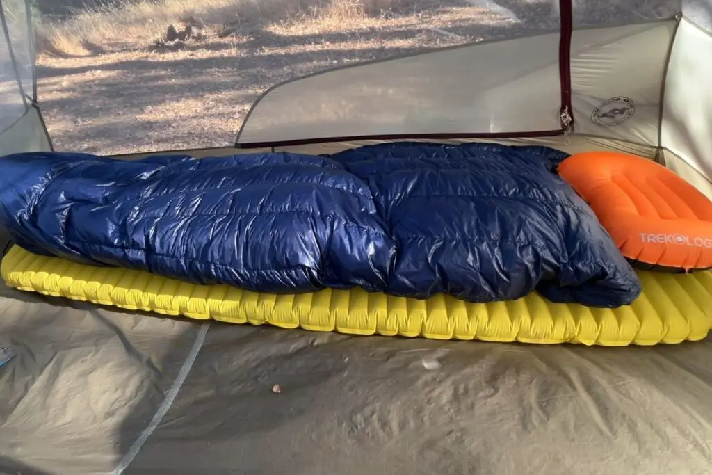 backpacking-sleep-pad-sleeping-bag-pillow Backpacking sleep system with a down quilt, inflatable sleeping pad, and inflatable pillow set up inside a tent