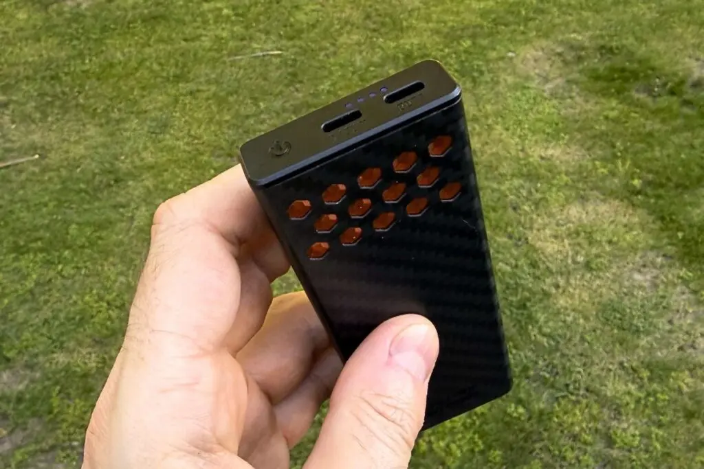 nitecore-carbo-10000-usb-c-ports 7:12 PMClaude responded: Hand holding the Nitecore Carbo 10000 Gen2, showing its carbon fiber shell with hexagonal ventilation cutouts and single USB-C port on top, outdoors over grass.Hand holding the Nitecore Carbo 10000 Gen2, showing its carbon fiber shell with hexagonal ventilation cutouts and single USB-C port on top, outdoors over grass.