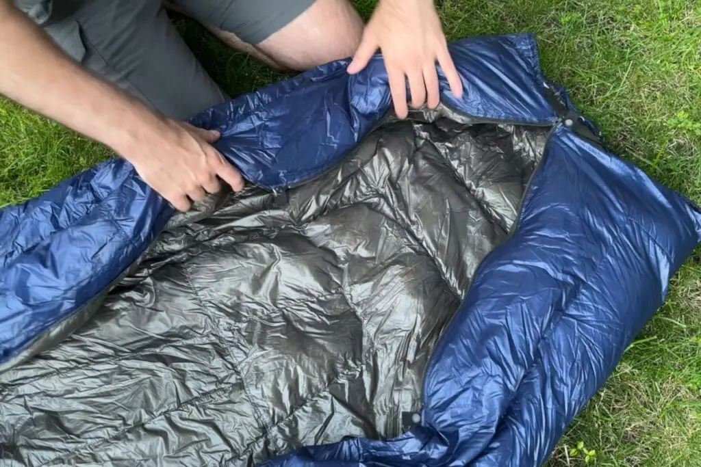 ultralight-backpacking-quilt-open-bottom Person opening the footbox of a navy blue backpacking quilt on grass, showing the open-bottom construction.