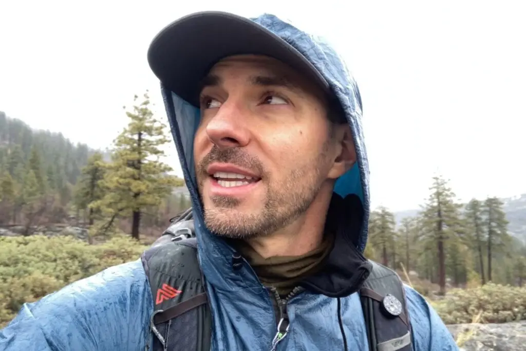 backpacker-wearing-frogg-toggs-rain-jacket A backpacker wears a hooded Frogg Toggs rain jacket while looking at the sky on a cloudy day in a backcountry clearing.