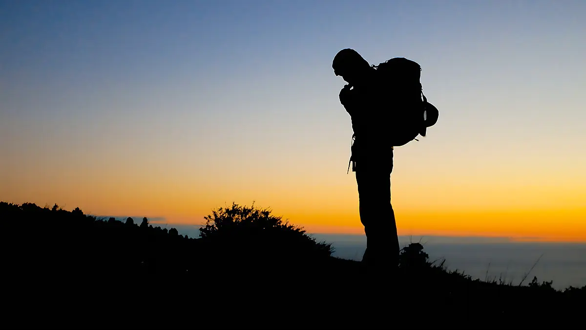 best backpacking first aid kits conclusion - Backpacker silhouetted against an orange sunset on a coastal ridge above the ocean