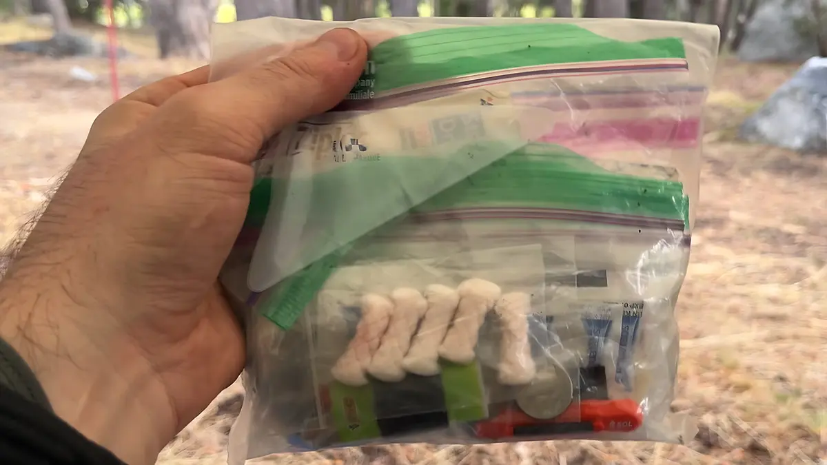 best backpacking first aid kits hero - Backpacker holding a homemade ziplock first aid kit packed with blister pads, medications and a whistle at a forest campsite