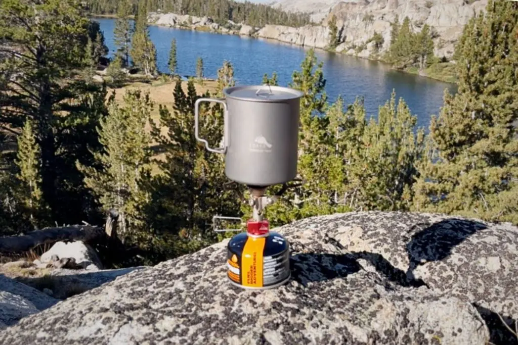 toaks-750-titanium-pot-backpacking-sierra-lake Titanium backpacking pot with lid on a canister stove atop a granite boulder, alpine lake and pines behind.